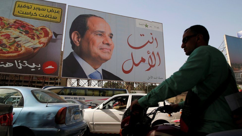 Ljudi šetaju ispred plakata egipatskoj predsednika Abdula Fateha el Sisija tokom pripreme za predsedničke izbore u Kairu, 25. marta 2018.