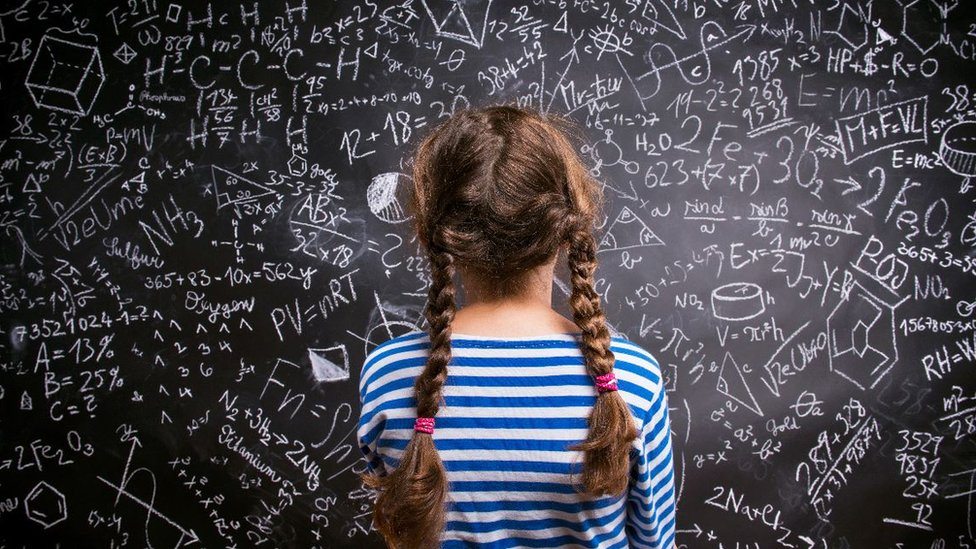 Girl looking at maths sums on a blackboard