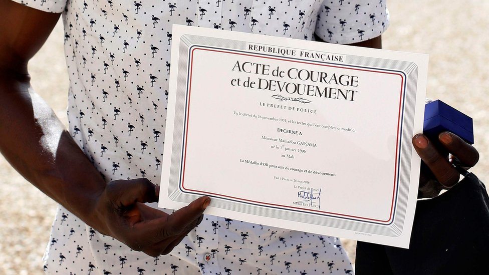 Mamudu Gasama pokazuje sertifikat koji je dobio zato što se popeo na zgradu i spasio dečaka