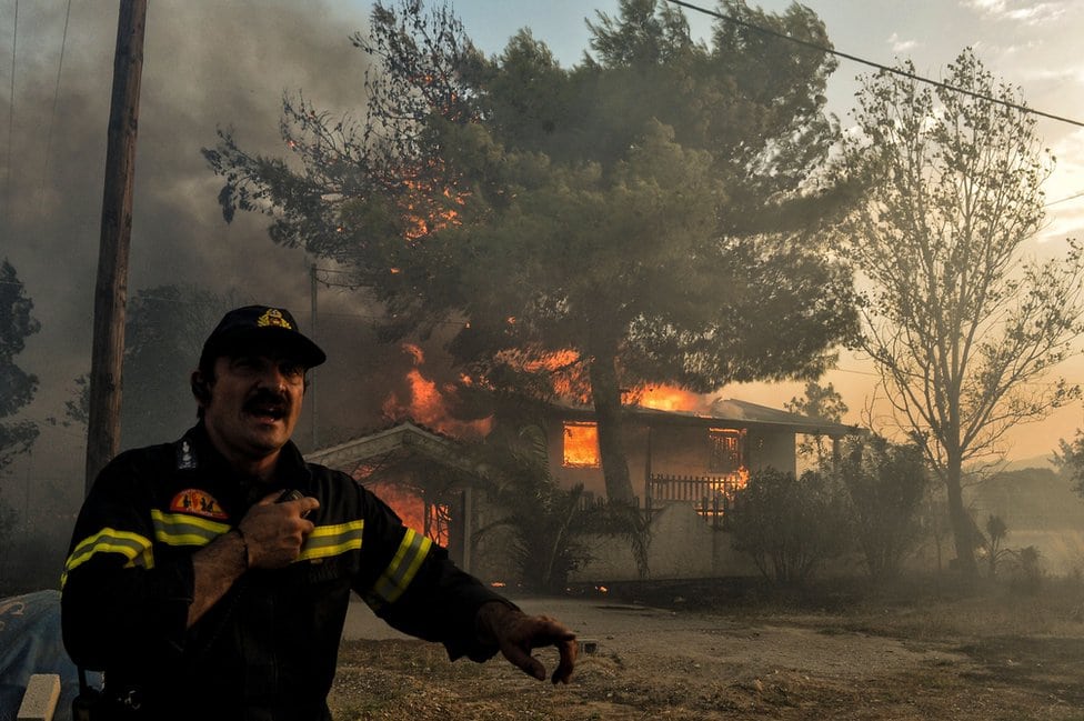Vatrogasac stoji ispred zapaljene kuće u Kineti, mestu pored Atine