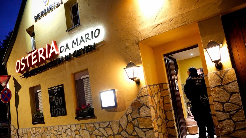 Znak na žutoj kući kaže da je u pitanju restoran Osterija Da Mario - ali dvojica policajaca čuvaju otvorena vrata na ovoj fotografiji