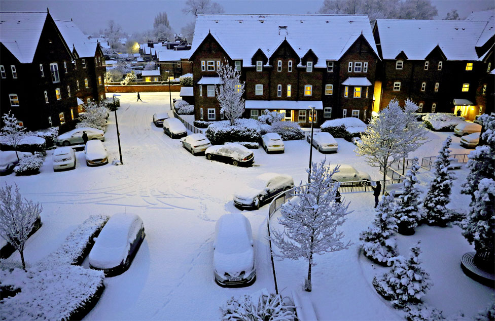 People walk along a snow covered road in Altrincham