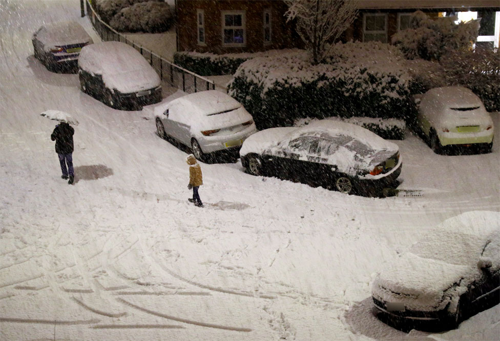 People walk along a snow covered road in Altrincham