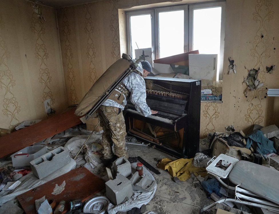 A soldier plays a piano in a damaged house