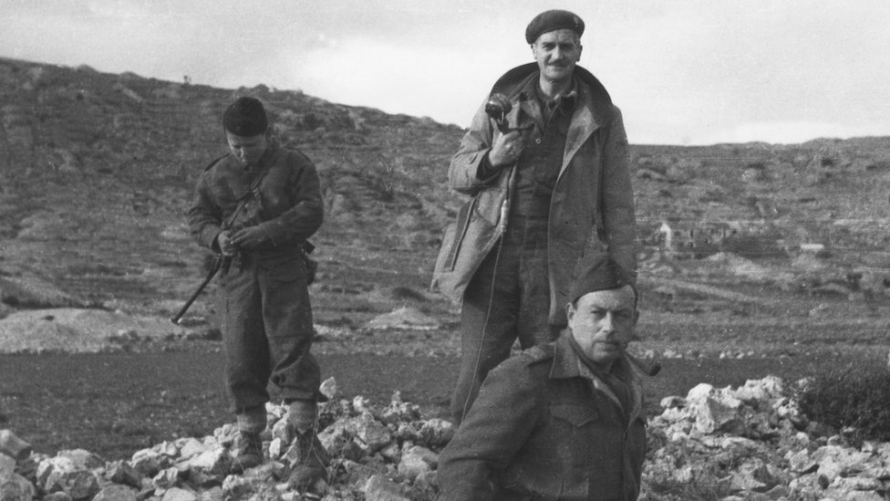 Denis Johnston with a boy who sang serbian songs in the progranmme. In March 1944 Denis Johnston, BBC War Correpondent visited Yugoslavian Partisans on an island off the coast of Yugoslavia. Recordings were made of a march past and of songs and speeches. Copyright: BBC