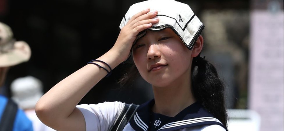 A Japanese high school student uses a handkerchief to cover her head from sunlight