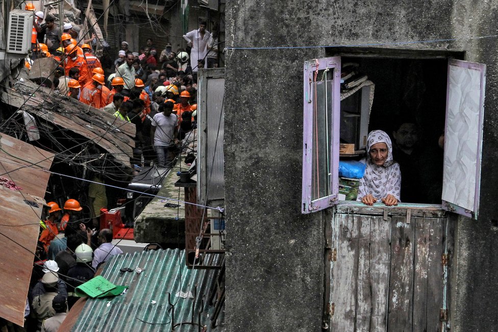 A resident looks out of her house as rescue workers search for survivors at the site of a collapsed building in Mumbai