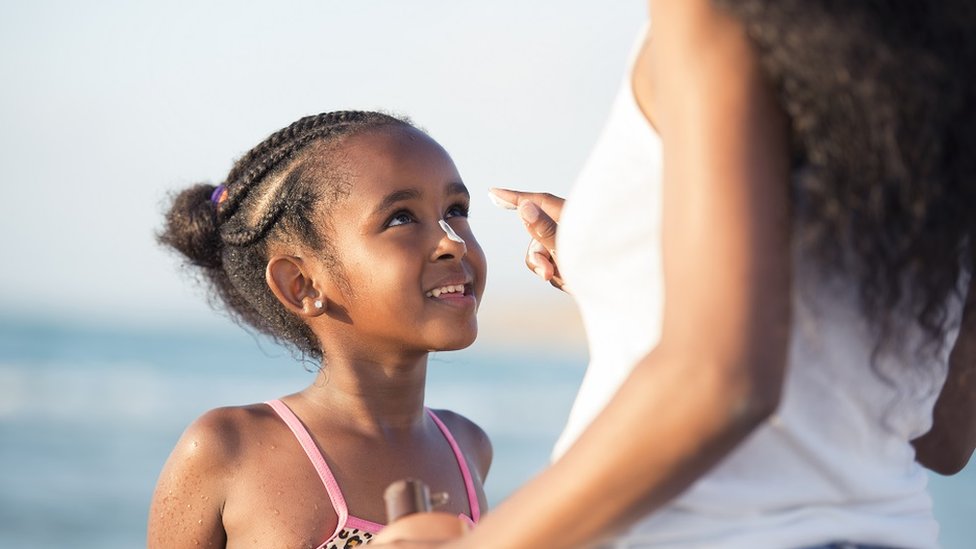 Mother applies sun protection cream to her six-year-old daughter on a beach