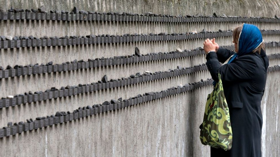 žena pali sveću na memorijalu