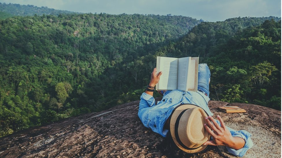 Kakav je uticaj čitanja na mentalno zdravlje 2 Young man relaxing and reading a book at the top of a rocky cliff, on holiday in Thailand.