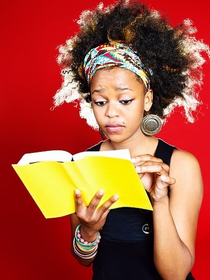 A worried-looking young woman reading a yellow-covered book.