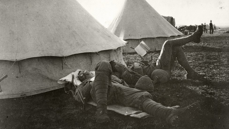Two British soldiers relaxing outside their tent. One of them is reading a book.