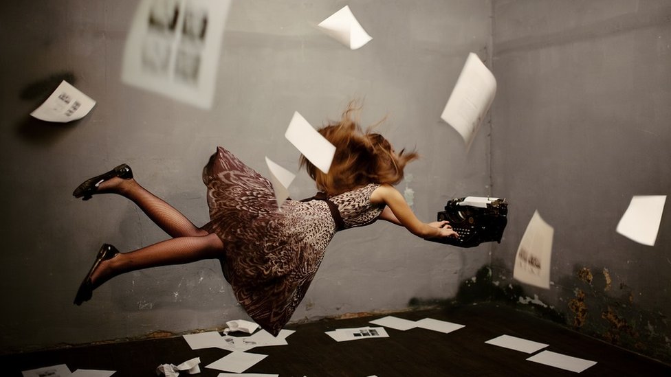 Kakav je uticaj čitanja na mentalno zdravlje 8 Surreal concept image: a young woman writing, suspended in mid-air, typing on a flying typewriter. There are pages on the floor and floating in the air around her.