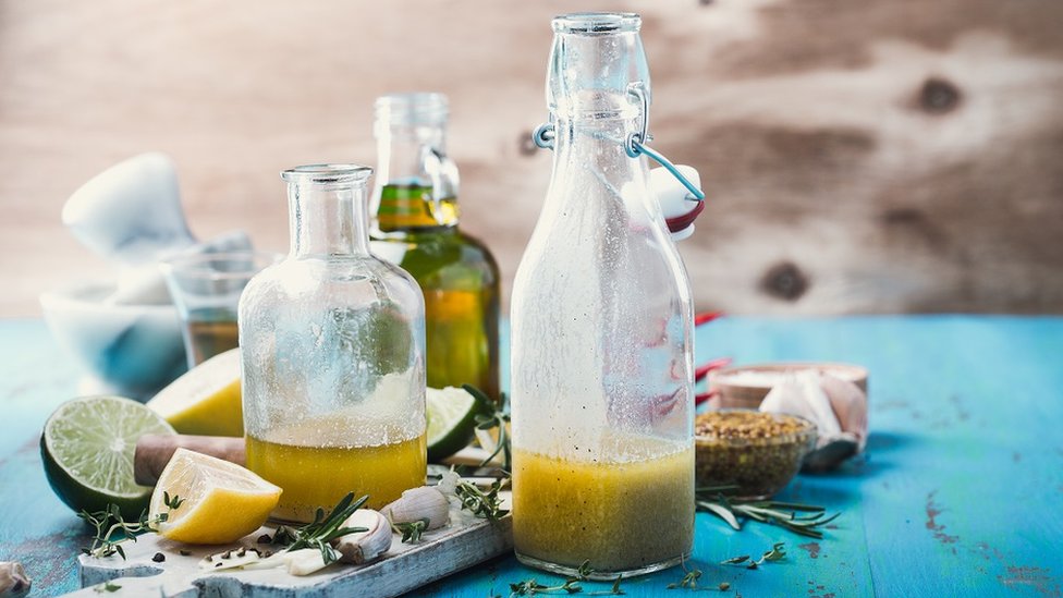 Glass bottles with with oil and vinegar on a wooden board. There are cloves of garlic, sprigs of thyme and slices of lime and lemon too.
