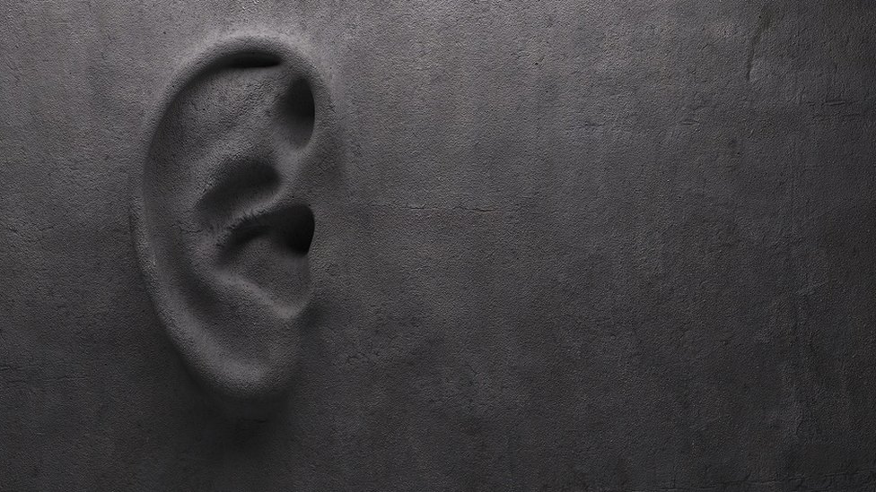 A grey concrete wall, with an ear sculpted in it - "ear on wall" concept.