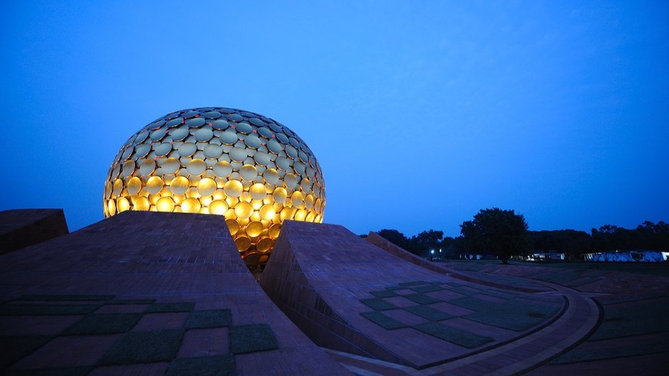 The Matrimandir at dusk: the building is a giant golden globe, over a dark blue sky.