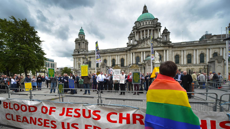 A man in a rainbow flag watches a Christian protest against the Belfast Pride parade