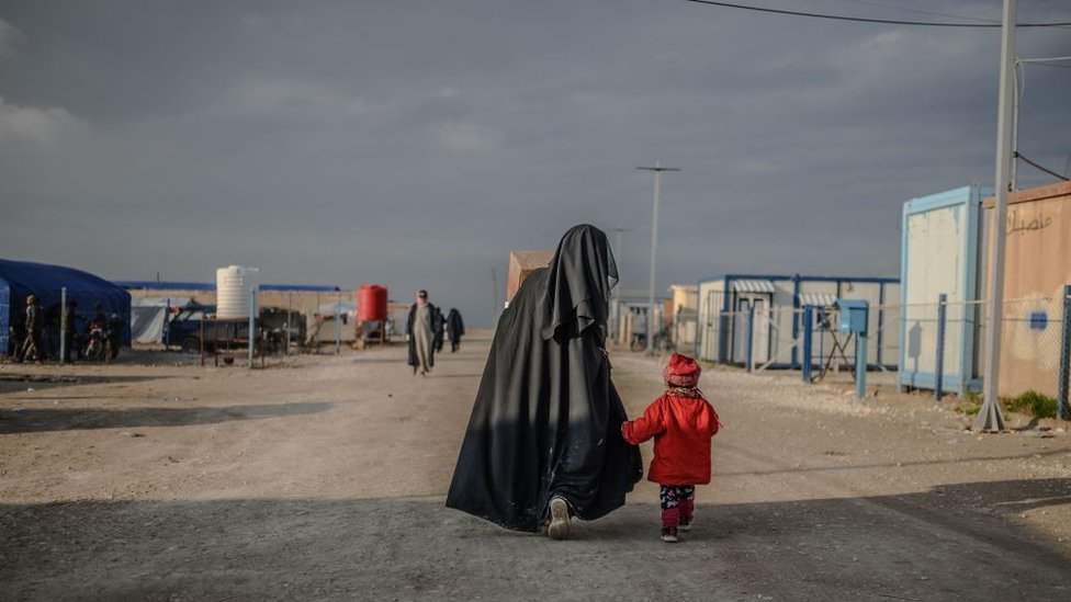 A veiled woman walks with her child at al-Hol camp