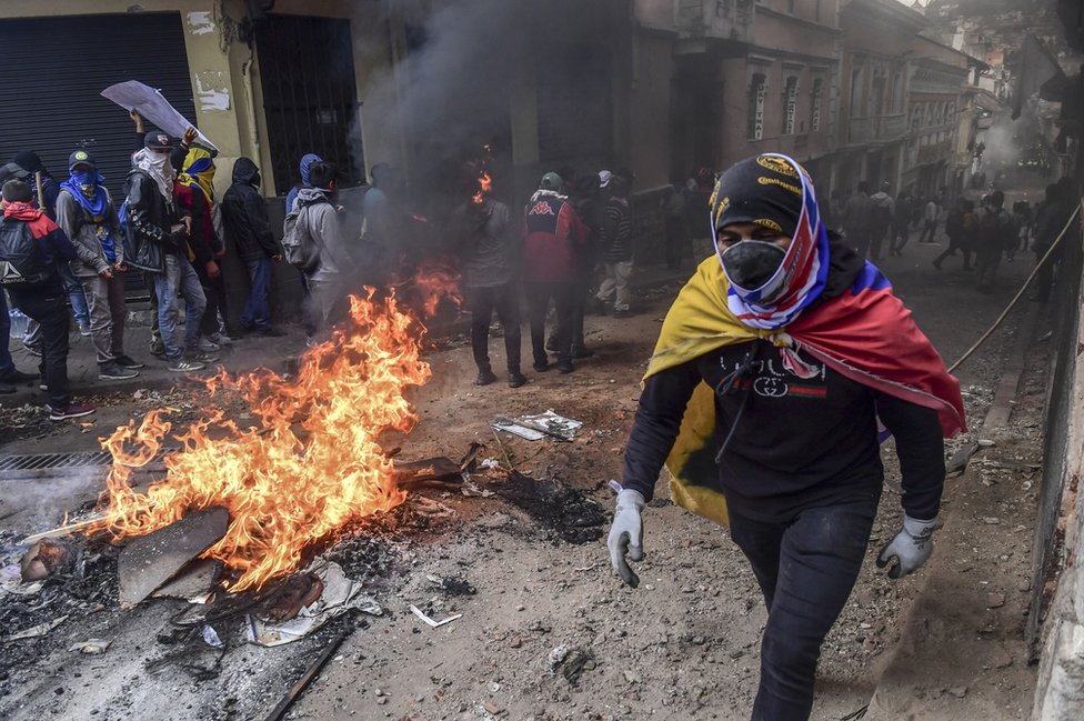 A demonstrator wrapped in an Ecuadorean flag passes by a barricade set on fire during clashes with riot police in Quito, as thousands march against Ecuadorean President Lenin Moreno's decision to slash fuel subsidies, on 9 October 2019.