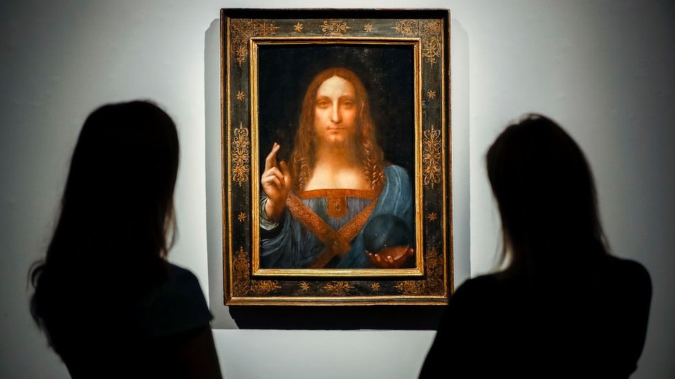 Staff members pose next to a painting by Leonardo da Vinci entitled Salvator Mundi before it is auctioned at Christie's in New York