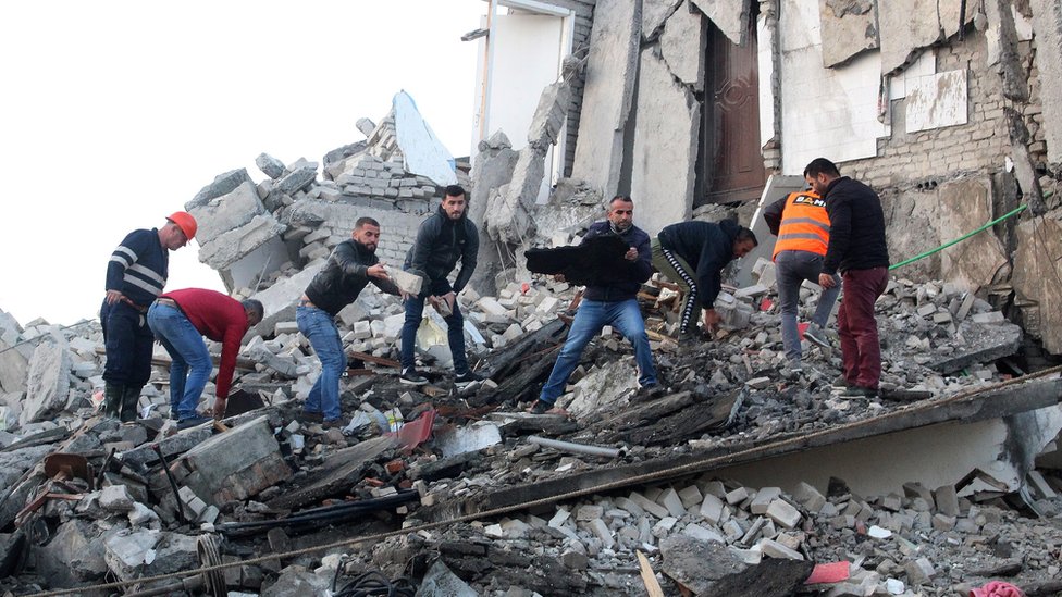 People stand on a collapsed building and move rubble