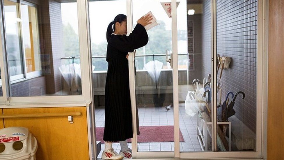 Japanese student cleans a glass door at her school