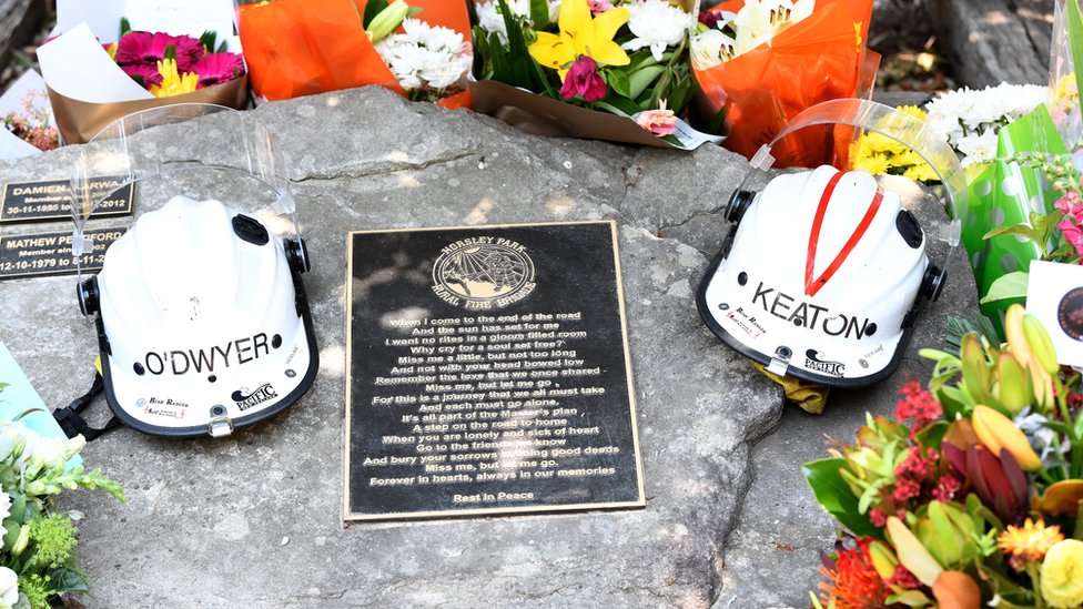 Požari u Australiji: Hiljade dobrovoljaca u borbi protiv plamena 5 Helmets of Andrew O'Dwyer and Geoffrey Keaton and flowers on their memorial at the Horsley Park fire brigade