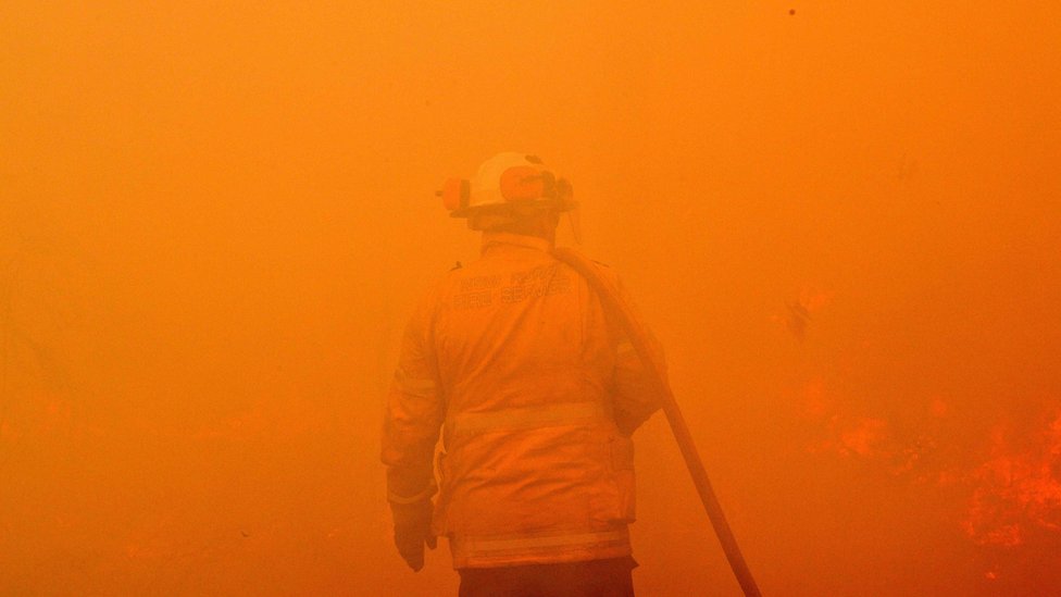 Požari u Australiji: Hiljade dobrovoljaca u borbi protiv plamena 4 A firefighter seen among the thick smoke and orange light of a bushfire near Sydney
