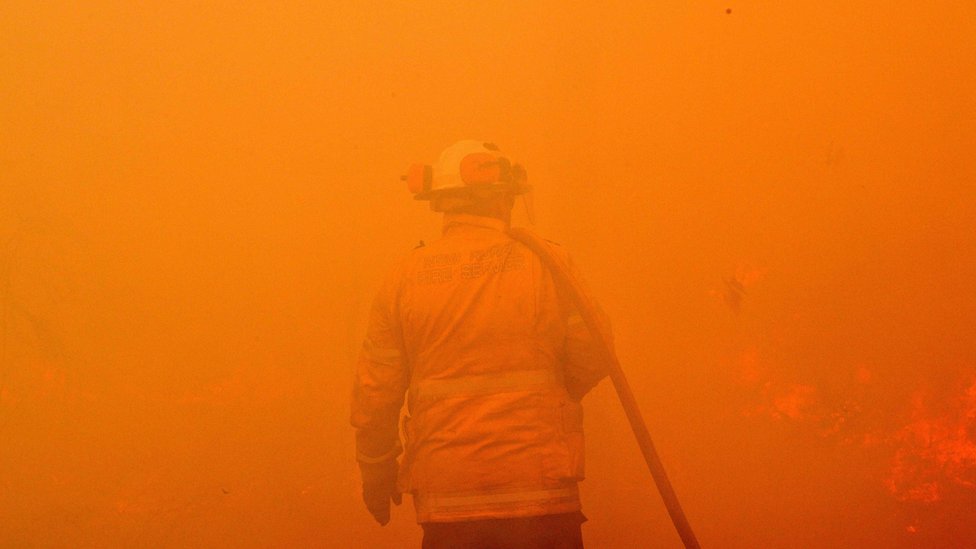 A firefighter seen among the thick smoke and orange light of a bushfire near Sydney
