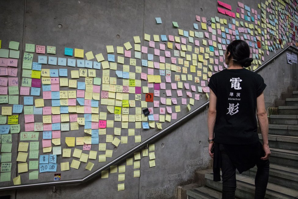 žena prolazi pored zida na kome su zalepljene poruke