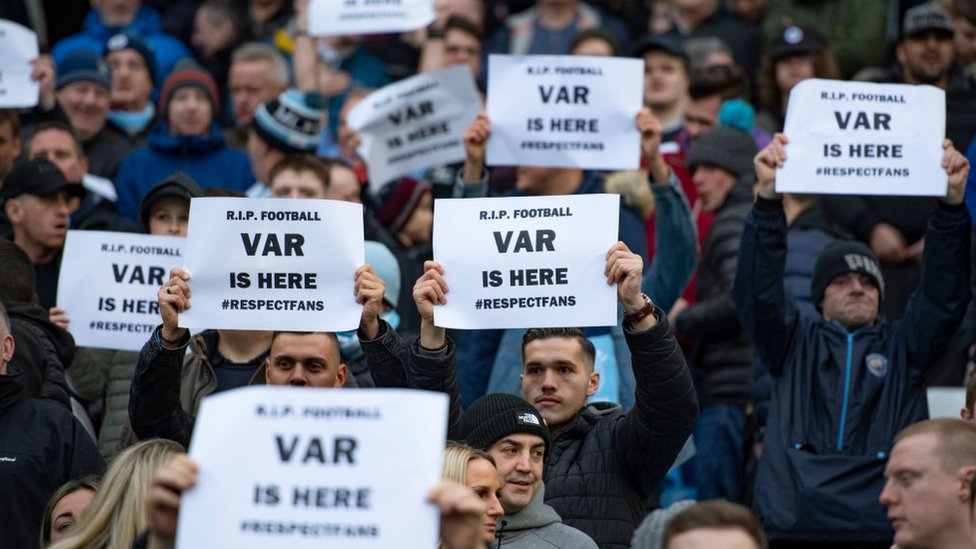 Fans hold up signs saying "VAR is here"