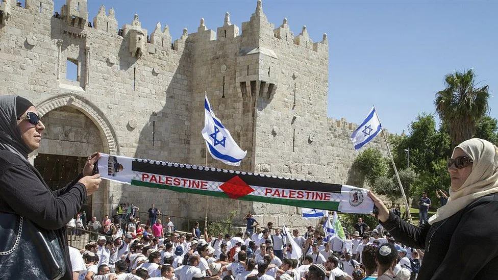 Izrael-Palestina: Tramp predstavio dugo očekivani plan za Bliski istok, PLO odbija 1 Palestinian women hold "Palestine" scarf as Israeli youth dance outside walls of Old City in Jerusalem (file photo)