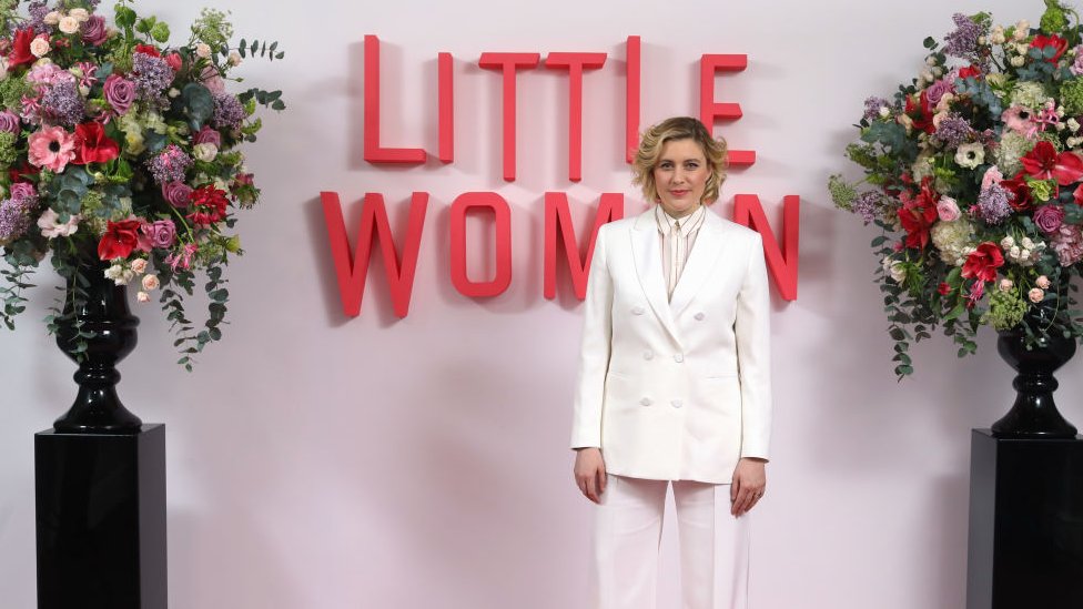 Greta Gerwig stood in front of a sign promoting Little Women