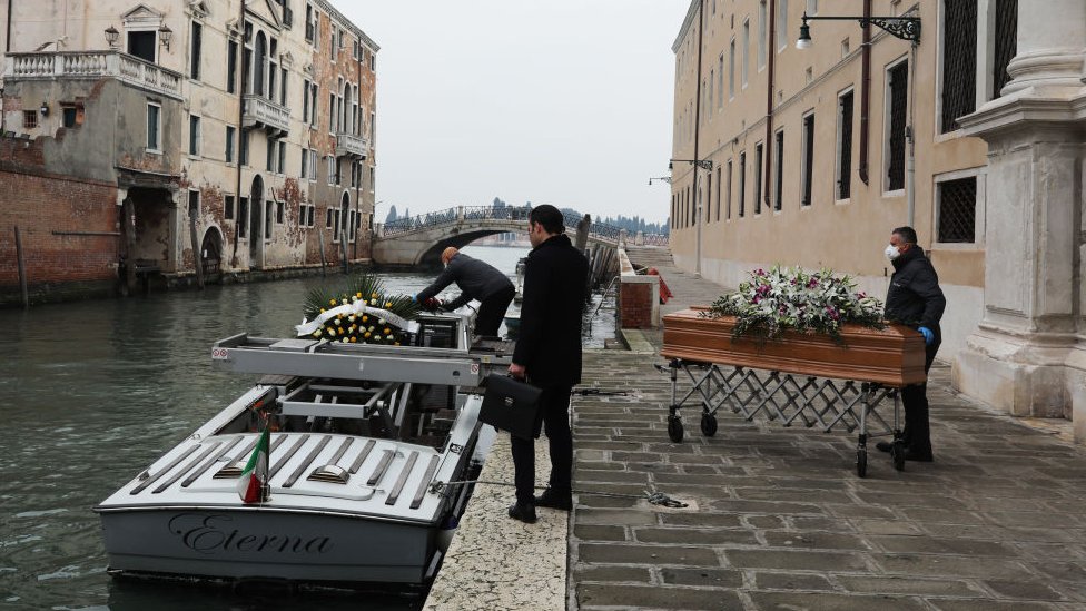 Undertakers place coffins on a boat in Venice