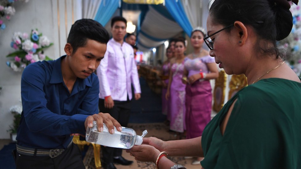 A man shares hand sanitiser with a woman at a wedding service in Cambodia