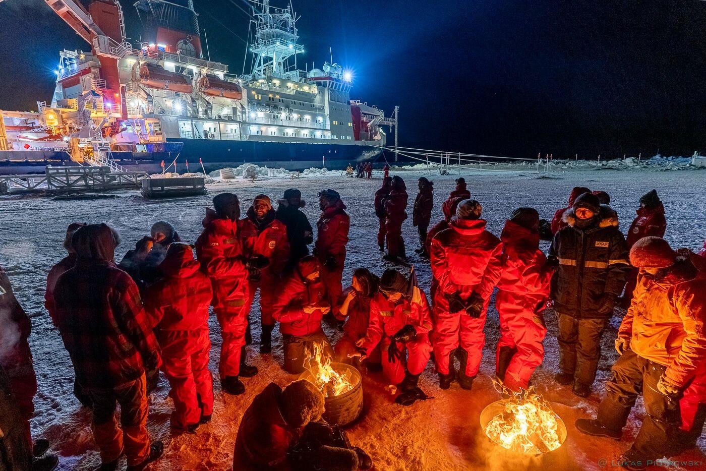 Researchers gathered around camp fire. Polarstern is seen in the background.