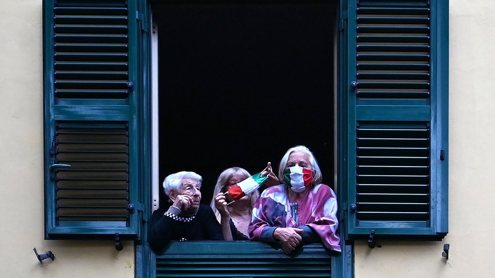 Korona virus: Još šest žrtava u Srbiji, poslanici se (ne)vraćaju u Skupštinu - u Nemačkoj maske obavezne 5 People with protective masks look from their windows at artists performing in the courtyard of a popular apartment building in Rome