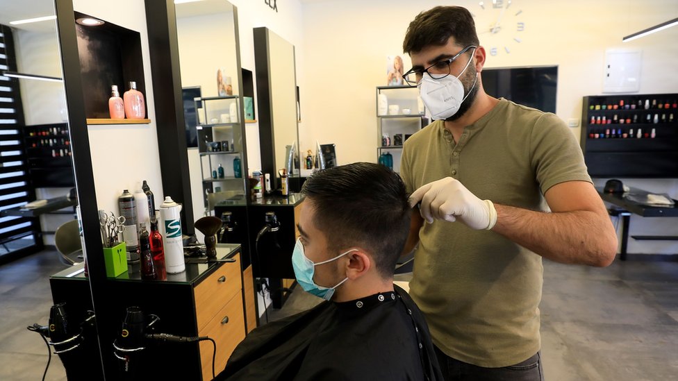 Kako kod frizera tokom epidemije korona virusa: „Zakazano sve do kraja maja, telefon mi se usijao" 1 A man cuts hair while wearing medical gloves and a high-grade face mask in a hairdressers' shop