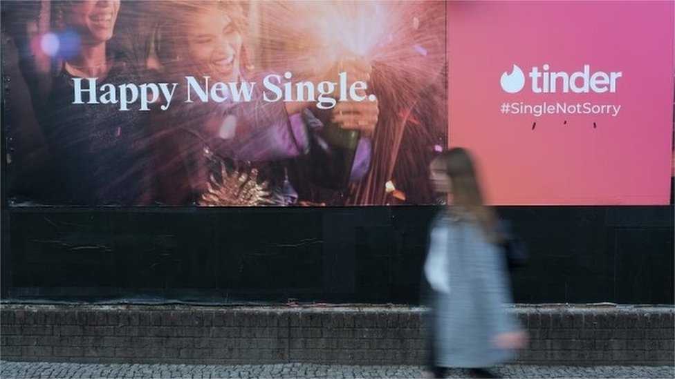 Mlada žena prolazi pored bilbord reklame za dejting aplikaciju Tinder
