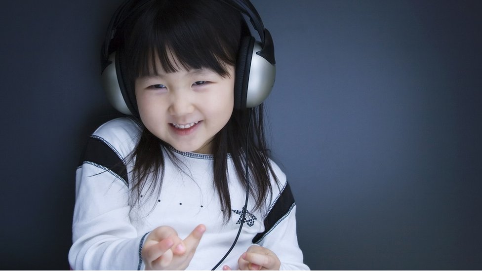 Child with headphones, fiddling with her fingers.