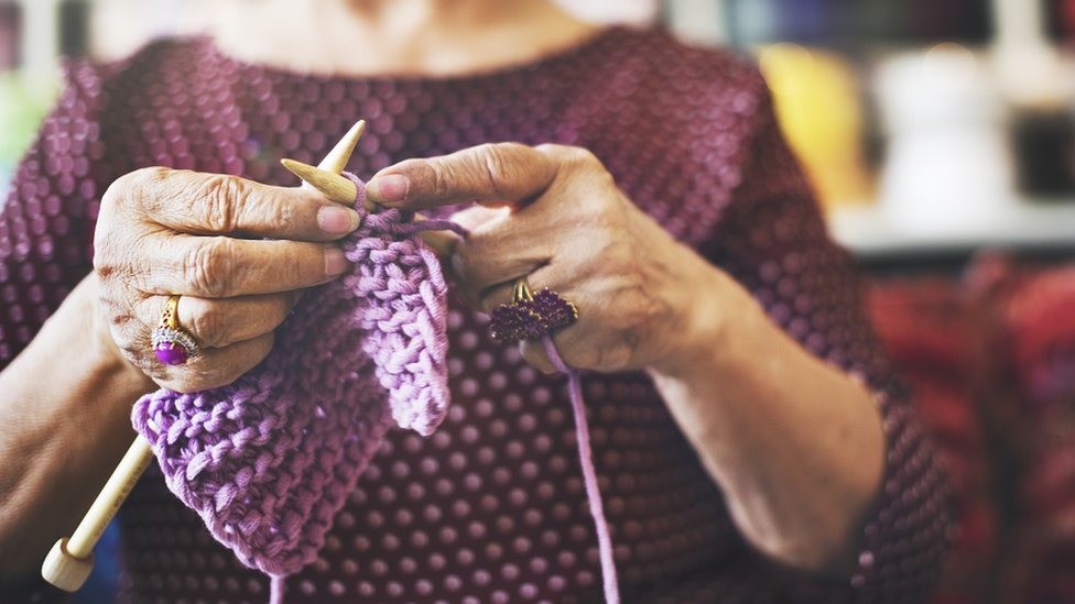 Woman with beautiful purple rings, knitting some purple yarn. She's wearing a purple top