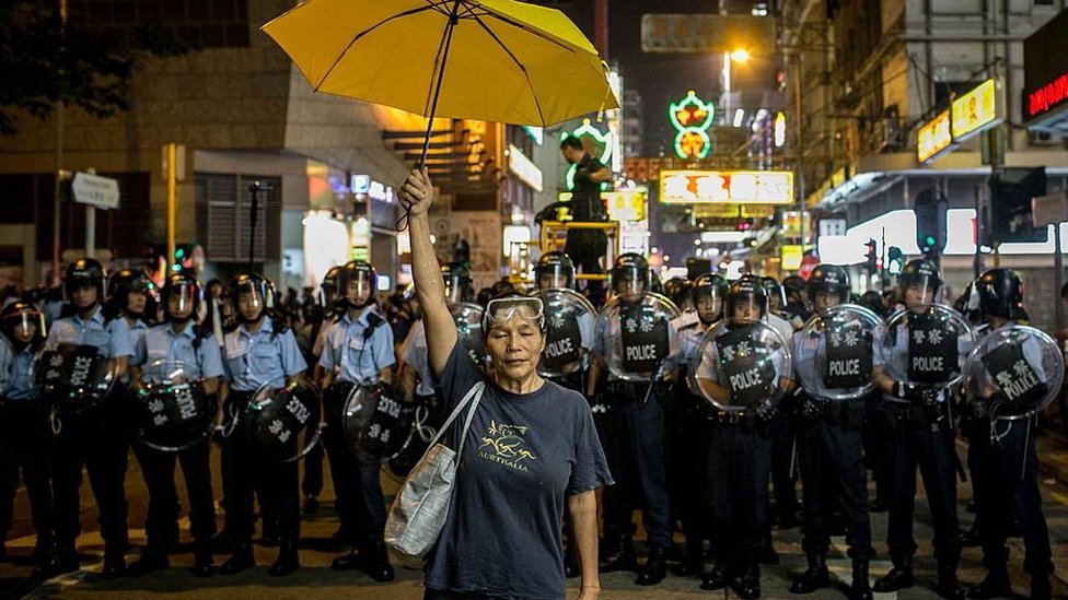 A pro-democracy activist holds a yellow umbrella in front of a police line on a street in Hong Kong in 2014