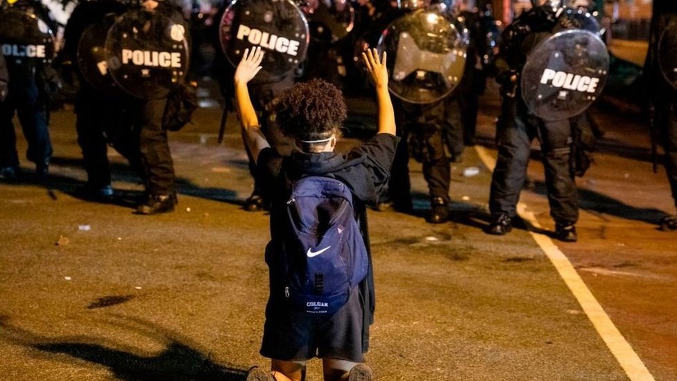 A demonstrator kneels and raises her hands facing a police line in front of the White House while protesting the death of George Floyd