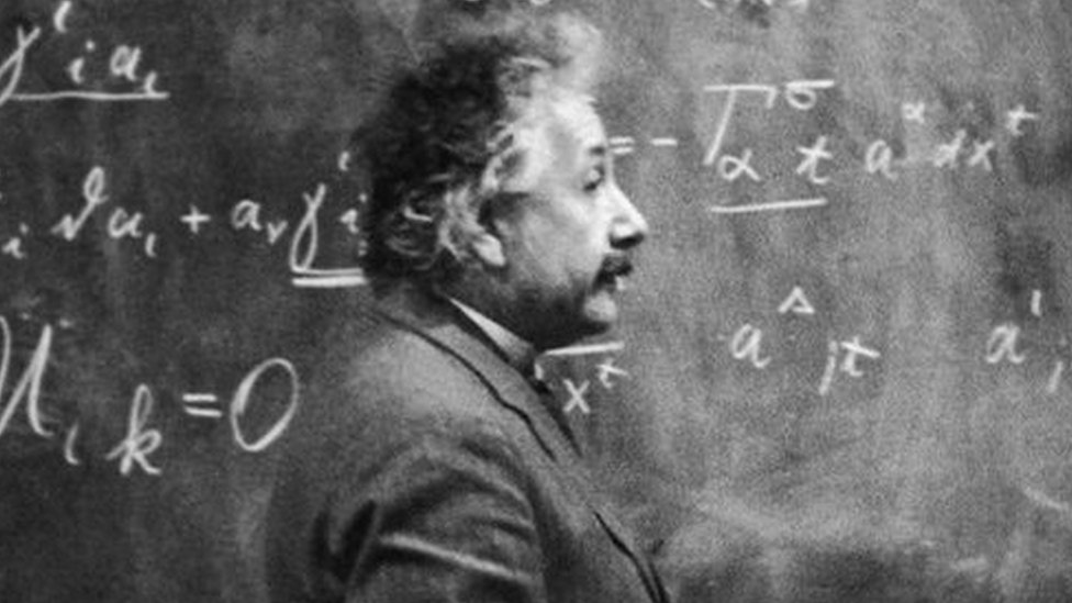 Albert Einstein standing beside a blackboard