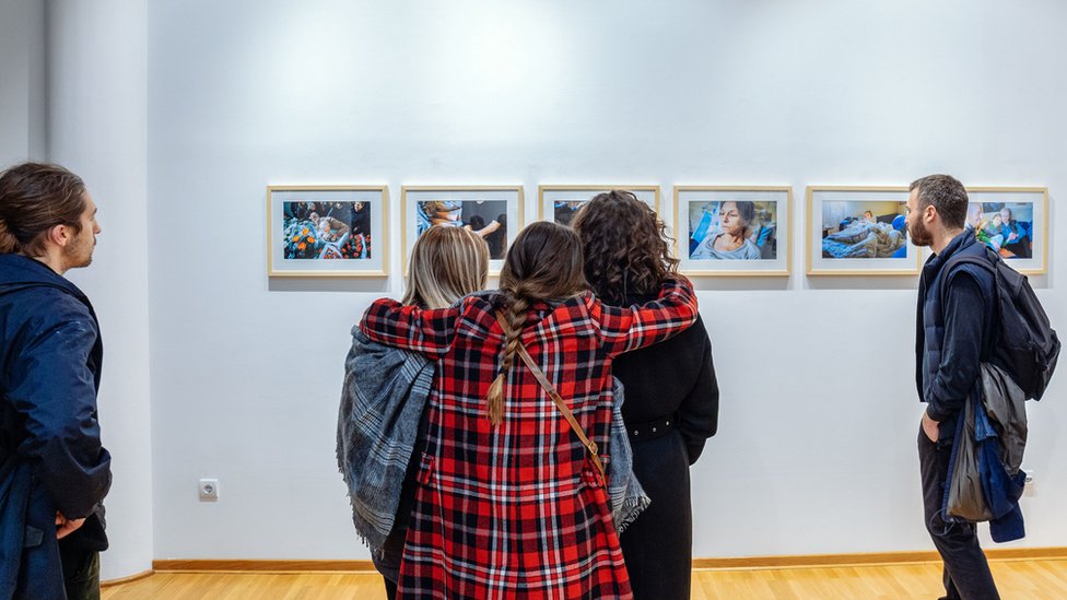 Devojke zagrljene posmatraju fotografije na izložbi