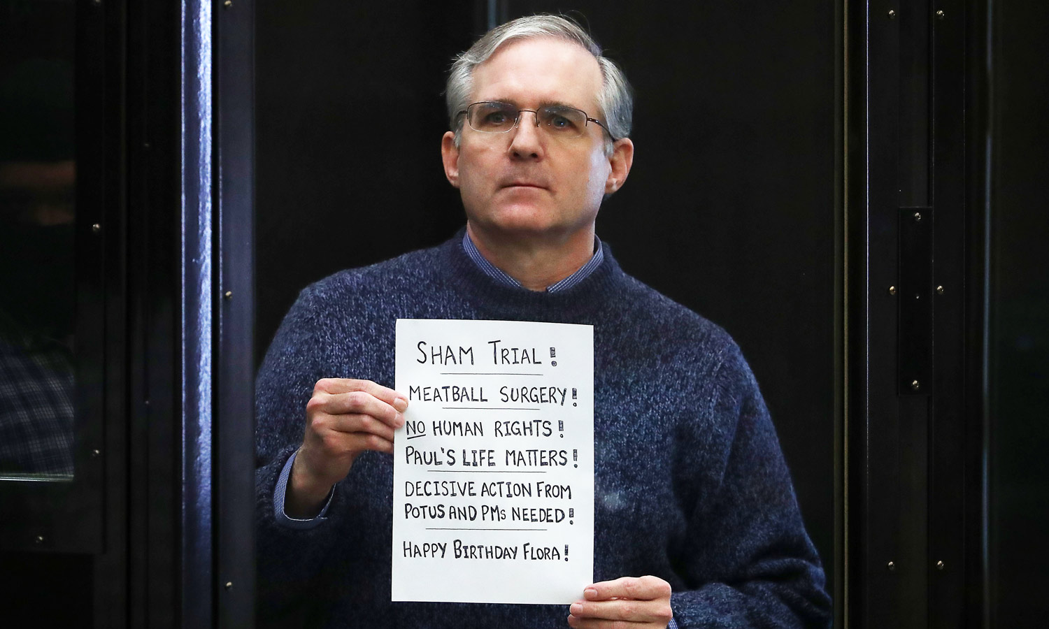 Paul Whelan holds up a sign at the end of his trial - "Sham trial! Meatball surgery! No human rights! Paul's life matters! Decisive action from potus and PMs needed! Happy Birthday Flora!"