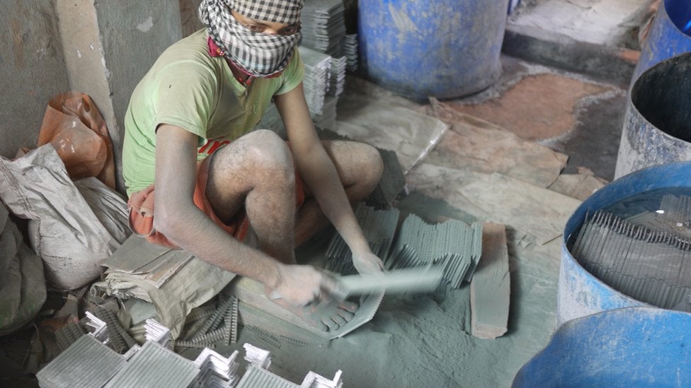 A worker at an informal recycling place clearing lead dust from battery parts