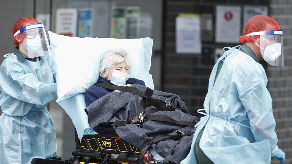 Healthworkers wearing full protective equipment wheel out an elderly patient