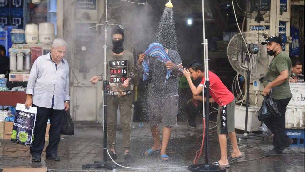 Iraqi men cool off under a public shower at a street in central Baghdad