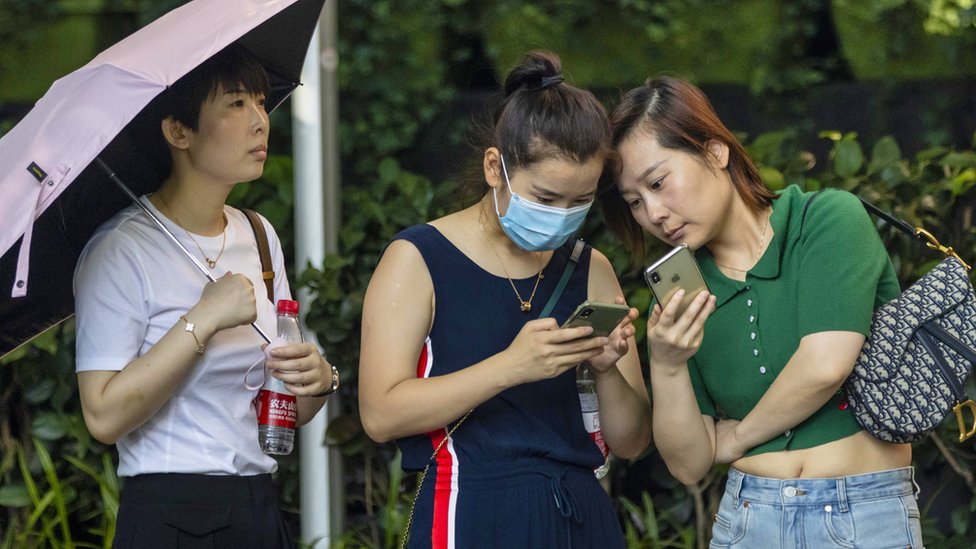 Two women look at mobile phones in the street in Shanghai